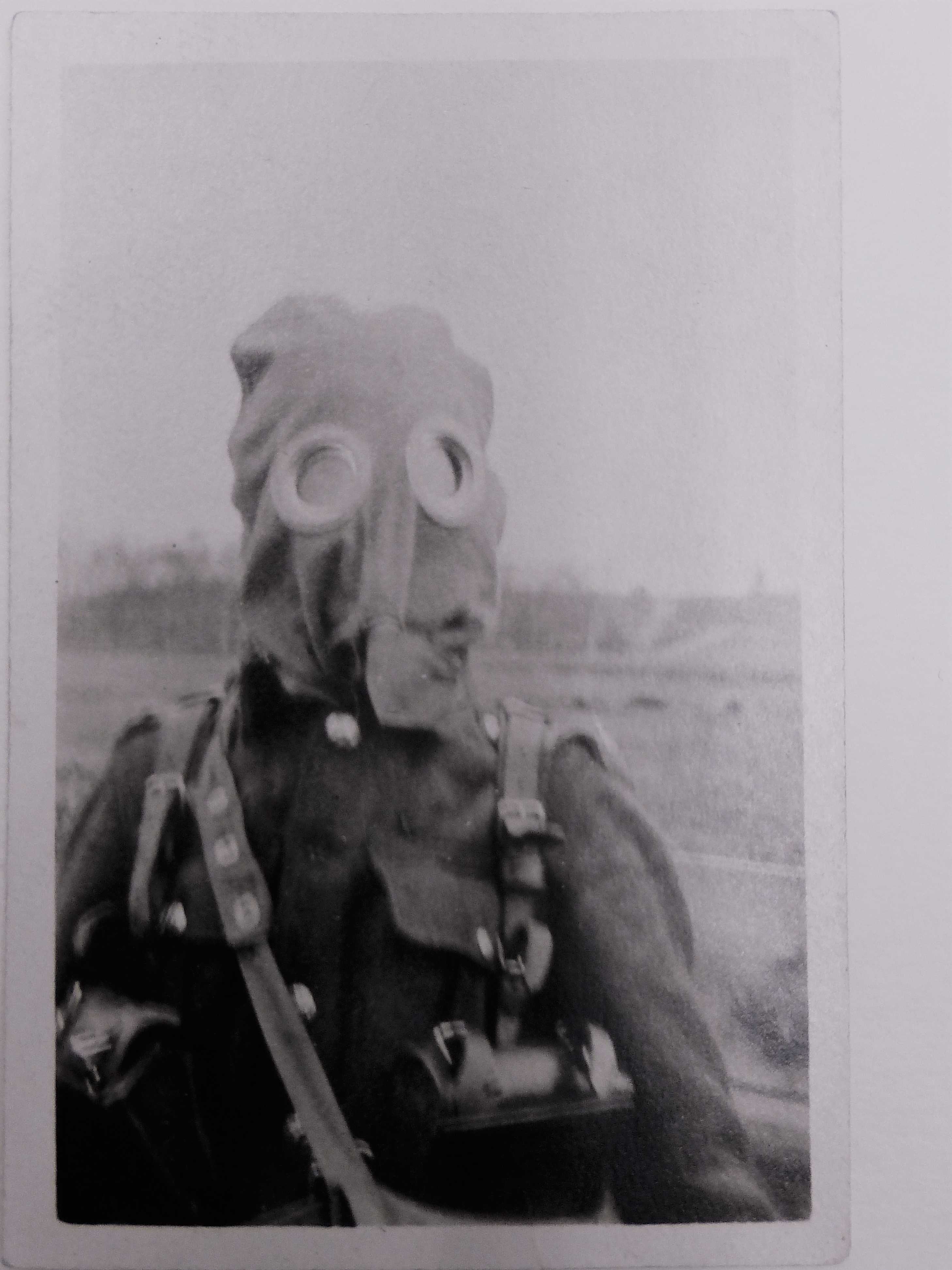 Image en noir et blanc d’un soldat en uniforme militaire portant un ancien masque à gaz. Le masque ressemble à un sac. Deux cercles en verre sont placés à la position des yeux.